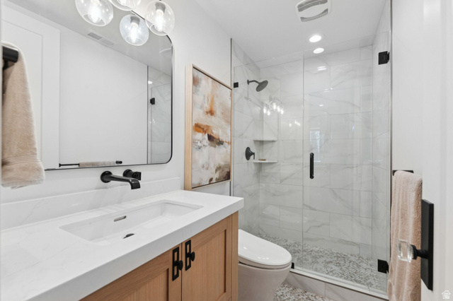 1400 Weber Wild Road Oakley, UT 84055 - Photo 39 of 55 Bathroom featuring a wall-mounted faucet, quartz countertop, wood-finish vanity, glass-enclosed shower with tile surround, and pebbled shower flooring