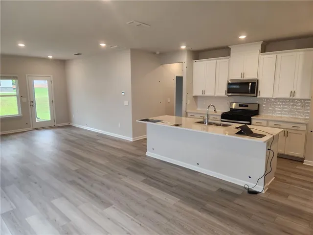 a kitchen with stainless steel appliances kitchen island granite countertop a stove a sink a refrigerator and white cabinets with wooden floor