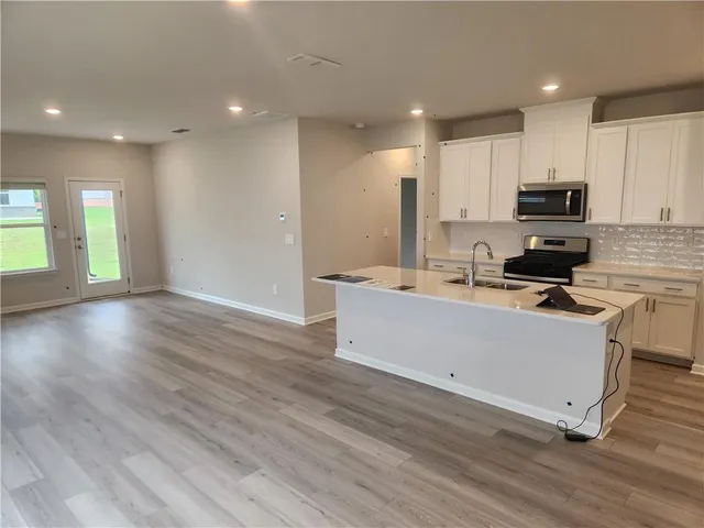 a room with kitchen island granite countertop a stove top oven a sink a counter space and cabinets