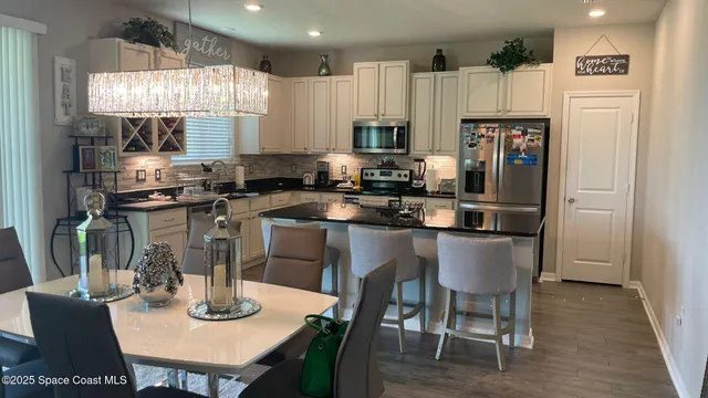 a kitchen with stainless steel appliances granite countertop a dining table chairs refrigerator and sink