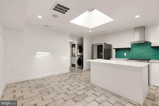 a living room with stainless steel appliances furniture a rug and a kitchen view