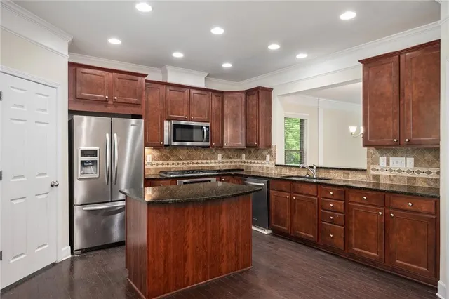 a kitchen with stainless steel appliances granite countertop wooden cabinets a refrigerator a sink a stove a microwave and wooden floors