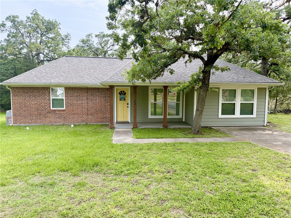 Single story home with roof with shingles, covered porch, a front yard, and brick siding