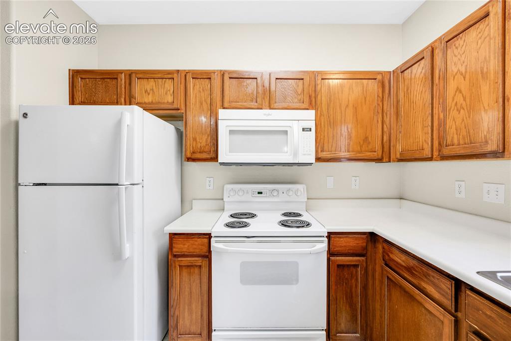 3864 Riviera Grove, Unit 102 Colorado Springs, CO 80922 - Photo 10 of 24 Kitchen featuring wood-finish cabinetry, white countertops, and white appliances including a refrigerator, range, and microwave