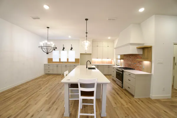 a kitchen with kitchen island a stove a chimney a sink and white cabinets