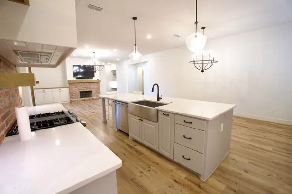 a large white kitchen with a stove a sink a refrigerator and white cabinets with wooden floor