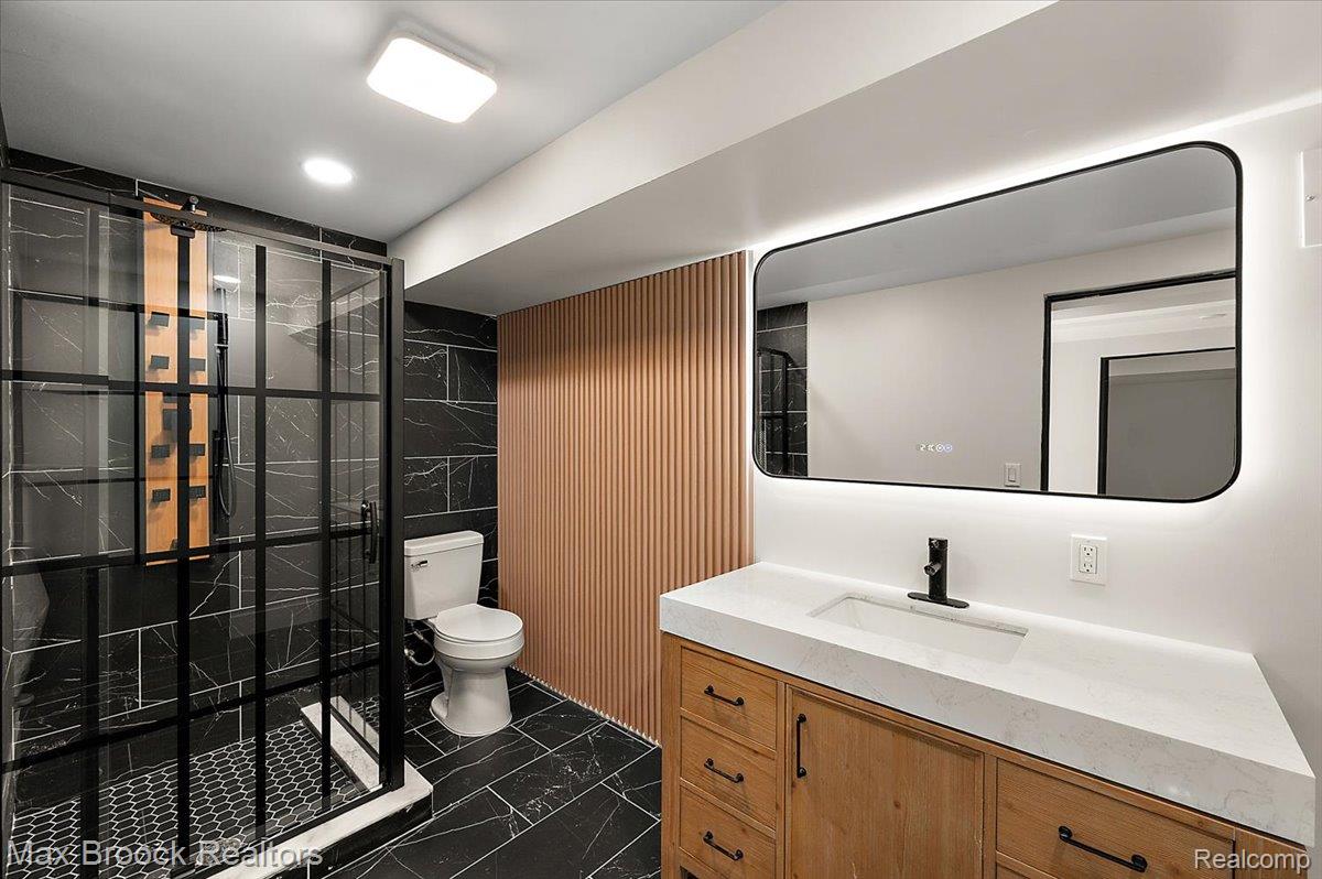 4597 Clarkston Road Clarkston, MI 48348 - Photo 46 of 74 Contemporary bathroom featuring a wood-finish vanity with an integrated sink, backlit rectangular mirror, and a black-framed glass shower enclosure