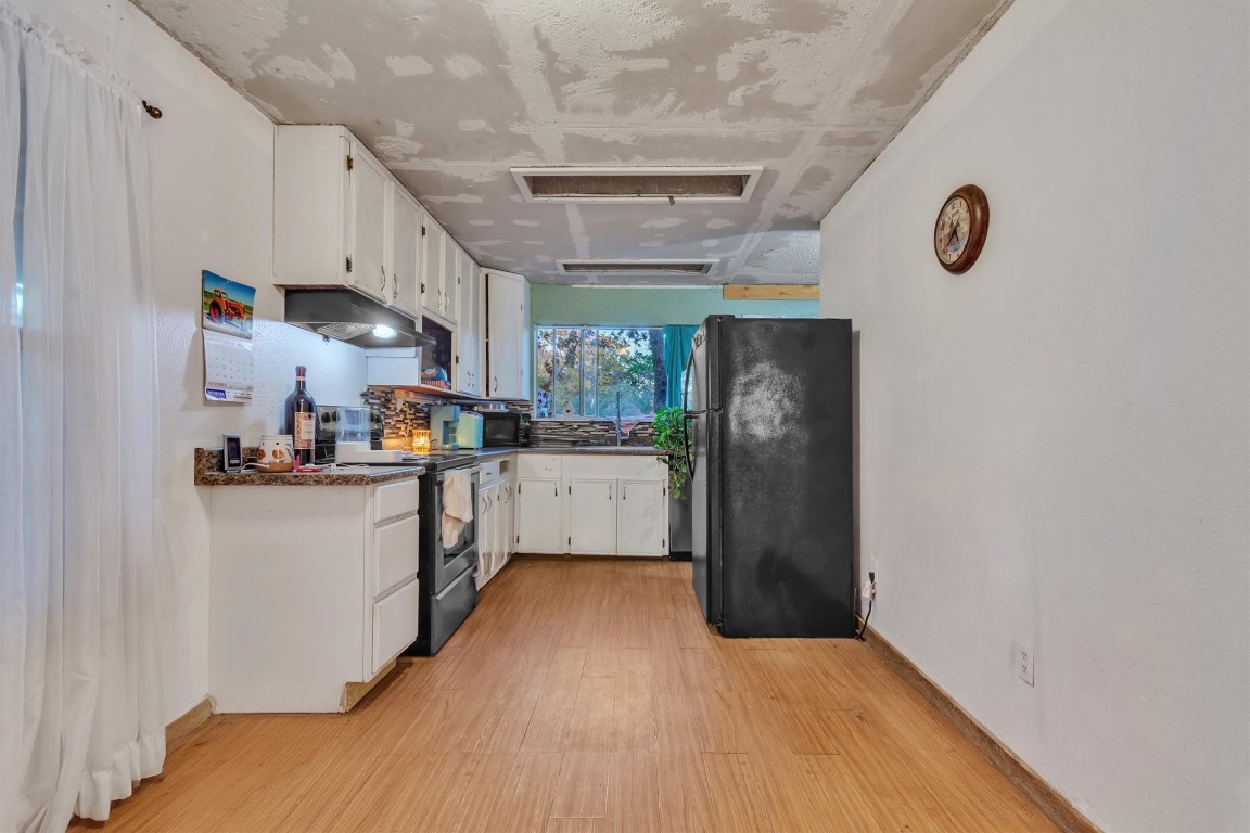 146 Wayside Drive Elgin, TX 78621 - Photo 8 of 24 Kitchen with white cabinetry, black appliances, light wood-type flooring, under cabinet range hood, and dark countertops