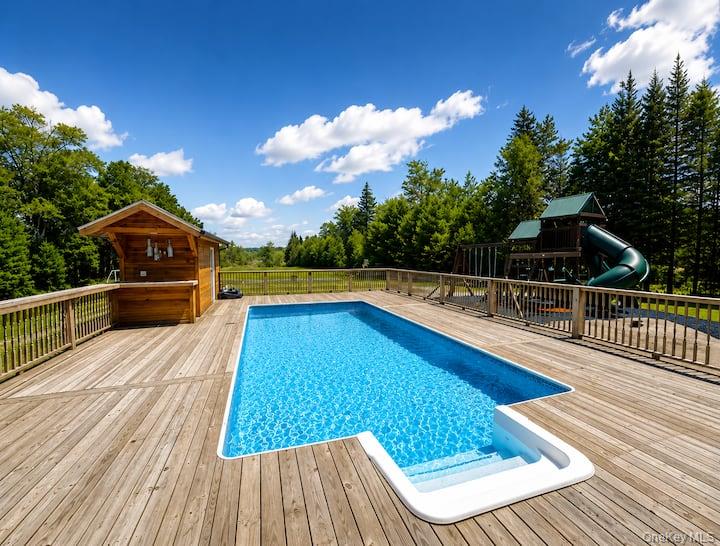 84 Mongaup Road Hurleyville, NY 12747 - Photo 5 of 50 Expansive outdoor deck featuring an in-ground swimming pool with built-in steps, a dedicated poolside bar structure, and surrounding wooded landscape