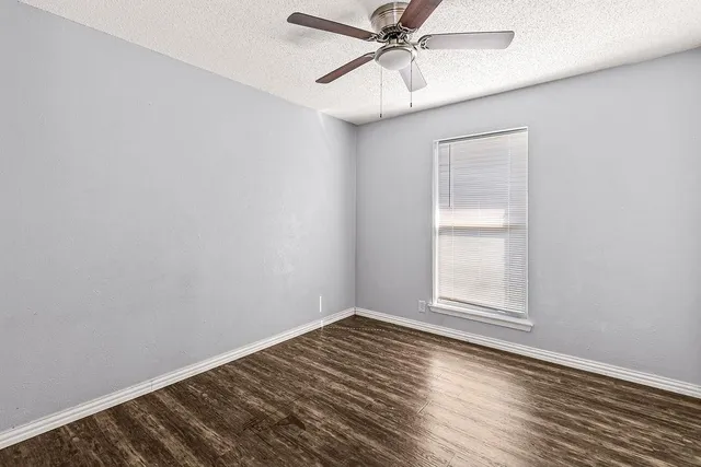 an empty room with wooden floor fan and windows