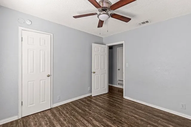 a view of an empty room with wooden floor and a ceiling fan