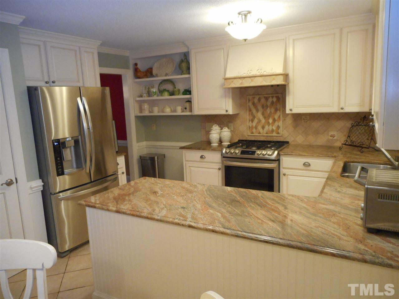 7920 Sutterton Court Raleigh, NC 27615 - Photo 3 of 22 a kitchen with granite countertop a refrigerator a sink dishwasher a stove and white cabinets with wooden floor