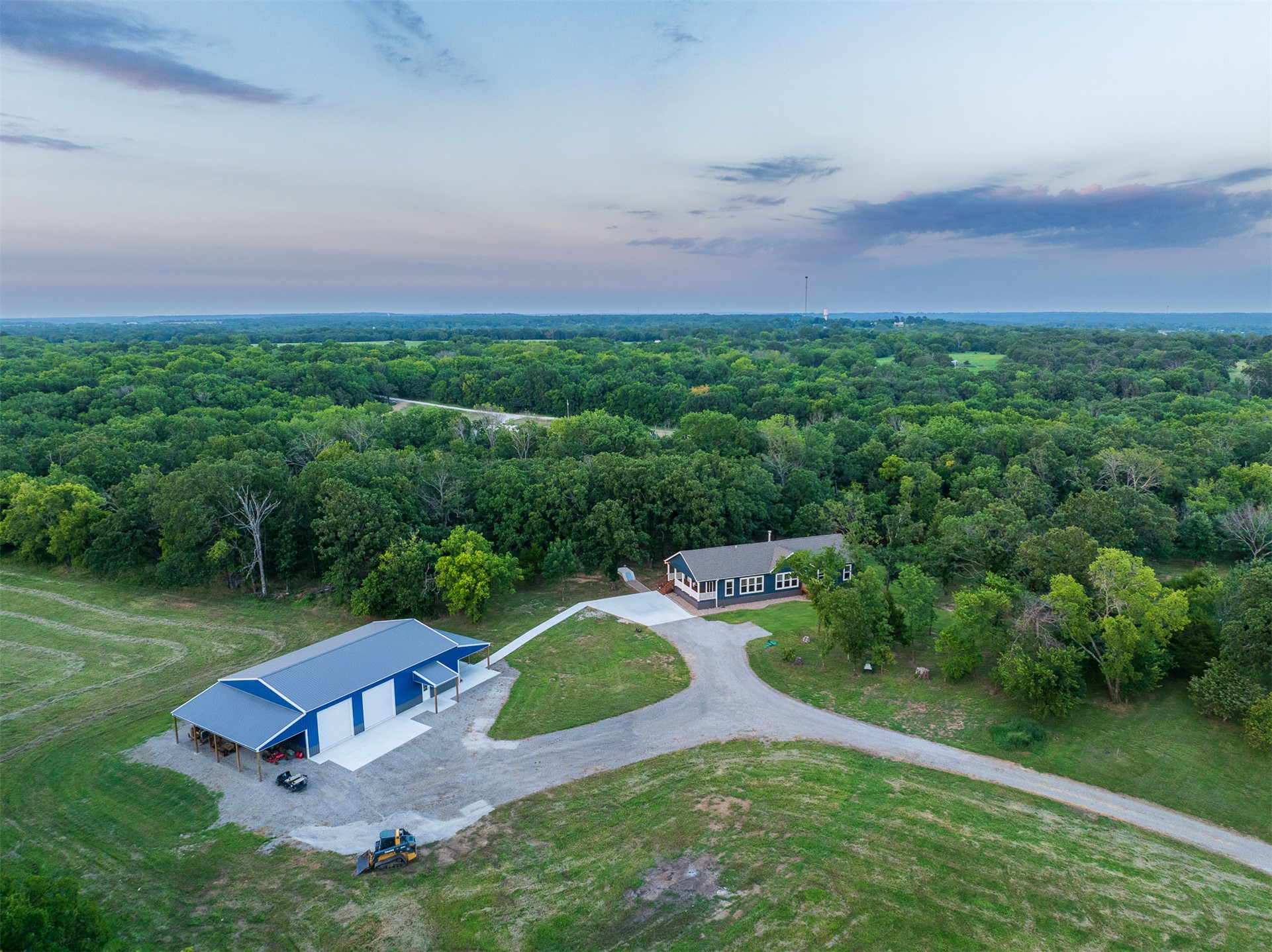 15291 East 400 Road Claremore, OK 74017 - Photo 2 of 96 Expansive property featuring a single-story residence, a large blue metal outbuilding with a covered porch, and a gravel driveway