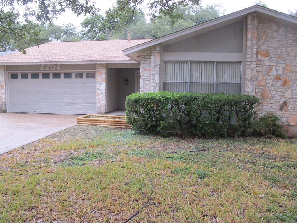 View of front of property with stone siding, a front yard, an attached garage, concrete driveway, and roof with shingles