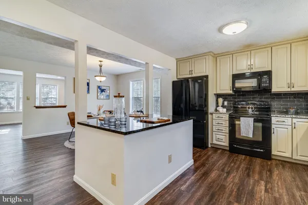 a kitchen with stainless steel appliances kitchen island granite countertop a refrigerator a stove a sink and white cabinets with wooden floor