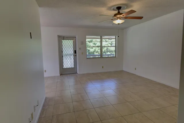 an empty room with chandelier fan and windows