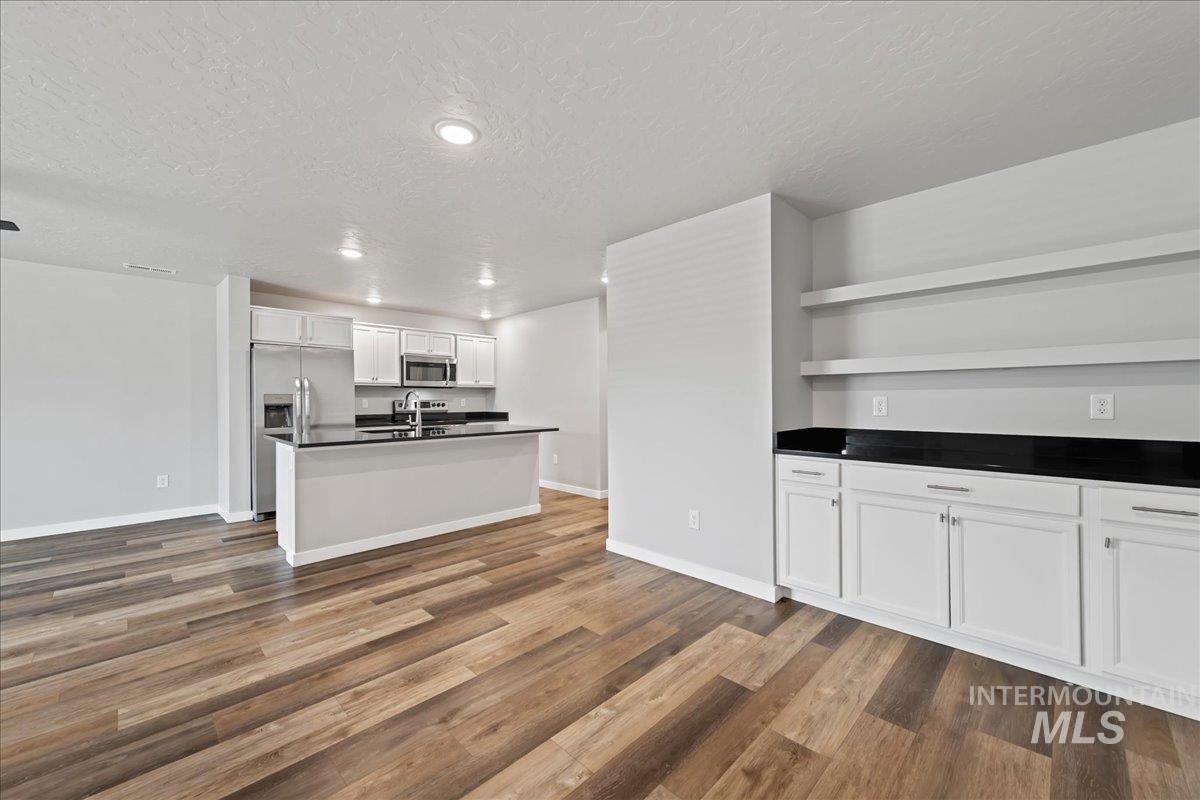 12535 West Victory Road Boise, ID 83709 - Photo 8 of 25 Open-concept kitchen with stainless steel appliances, an island featuring a sink, recessed lighting, and wood-finish flooring