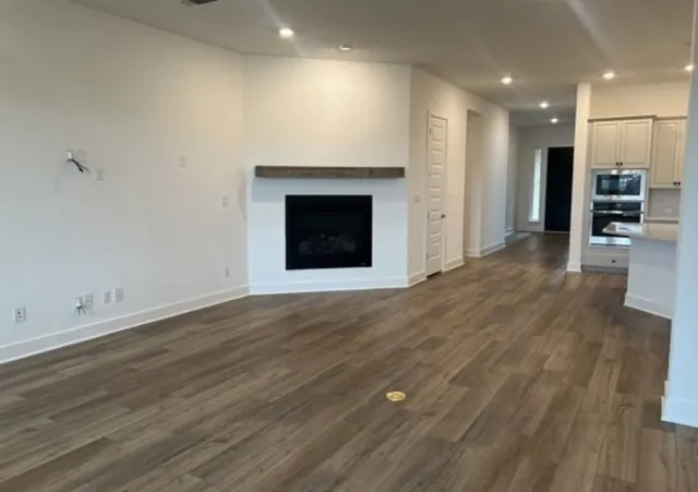 an empty room with wooden floor kitchen view and a fireplace