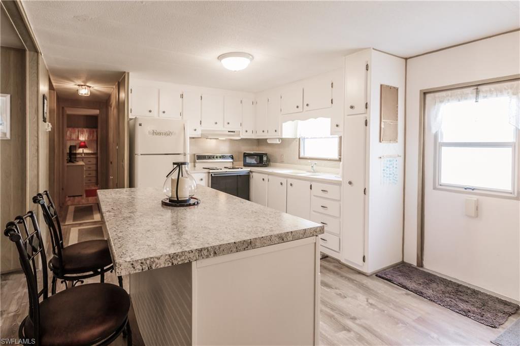 10100 Burnt Store Road, Unit 104 Punta Gorda, FL 33950 - Photo 13 of 46 Kitchen featuring a kitchen breakfast bar, a healthy amount of sunlight, white appliances, and and luxury vinyl plank flooring