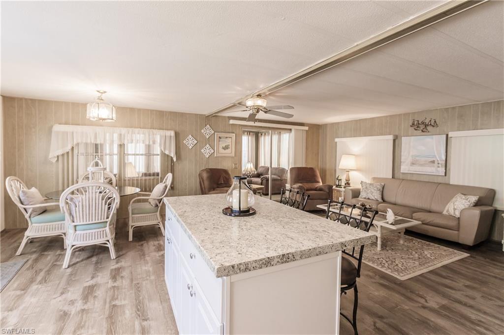 Kitchen featuring white cabinetry, a center island, wood-type flooring, a breakfast bar, and ceiling fan with dining area