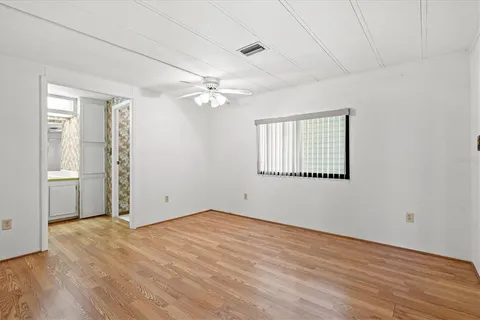 an empty room with wooden floor chandelier fan and windows