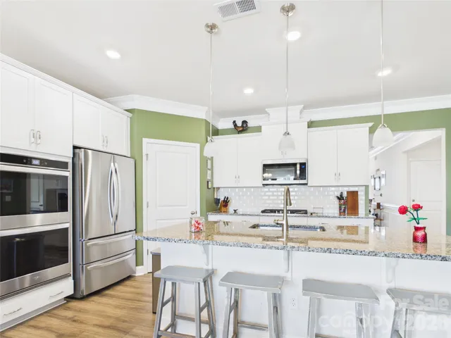 a kitchen with kitchen island granite countertop a sink cabinets stainless steel appliances and wooden floor