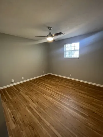 an empty room with wooden floor fan and windows