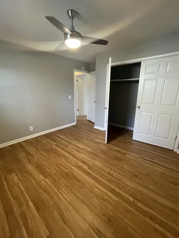 a view of an empty room with wooden floor and a ceiling fan