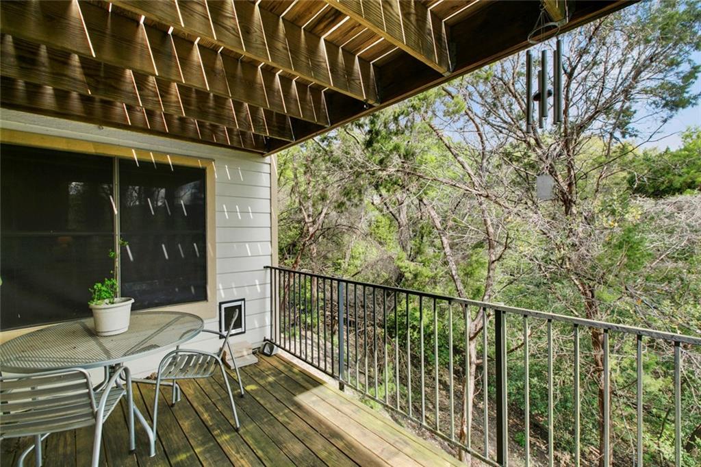 9201 Simmons Road, Unit 117 Austin, TX 78759 - Photo 11 of 11 Wood deck balcony with metal railings and a natural tree-lined backdrop