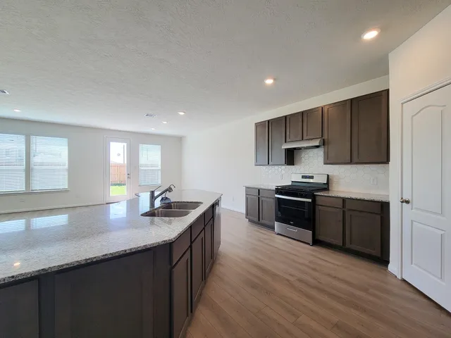 a kitchen with stainless steel appliances granite countertop a sink dishwasher a stove and a refrigerator with wooden floor