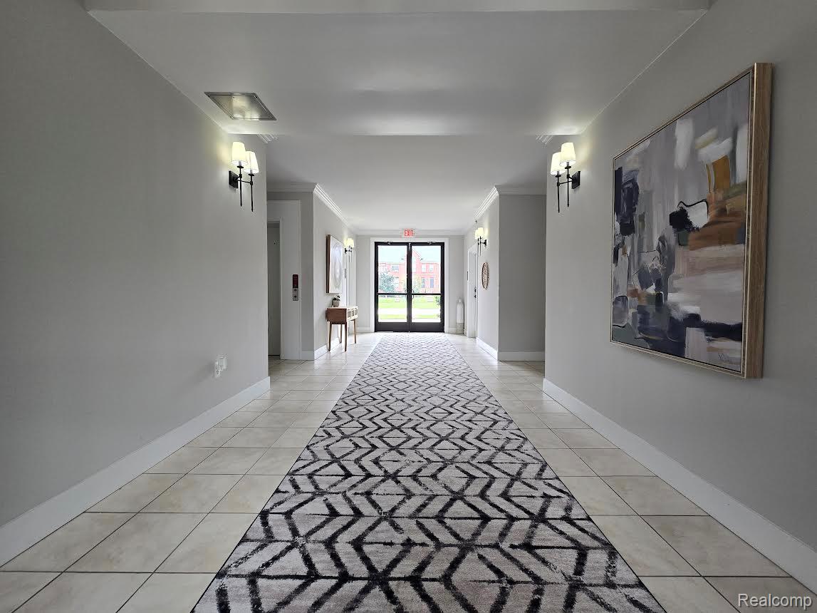 2727 East Maple Road Birmingham, MI 48009 - Photo 8 of 29 Hallway featuring wall sconce lighting, crown molding, a tiled floor, and a full-light glass door