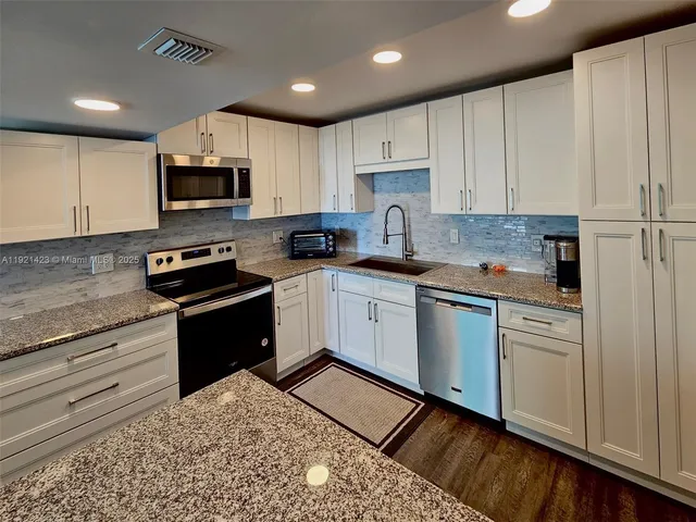 a kitchen with granite countertop a sink a counter top space stainless steel appliances and cabinets