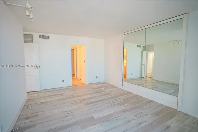 a view of an empty room with wooden floor and a bathroom