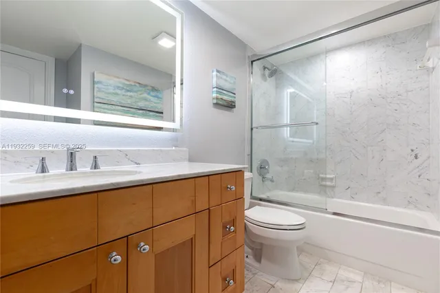 a bathroom with a granite countertop bathtub shower sink vanity and toilet