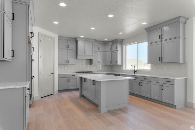 562 West Coyote Rdg Road Grantsville, UT 84029 - Photo 13 of 27 Contemporary kitchen featuring light wood-finish flooring, ample grey cabinetry with black hardware, white countertops, a tiled backsplash, and recessed lighting