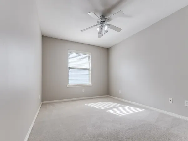 an empty room with a chandelier fan and windows