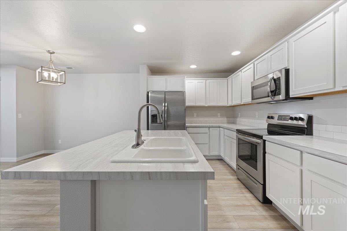 2479 East Goldstone Street Meridian, ID 83642 - Photo 12 of 29 Kitchen with stainless steel appliances, light countertops, light wood-style flooring, a kitchen island with sink, and pendant lighting
