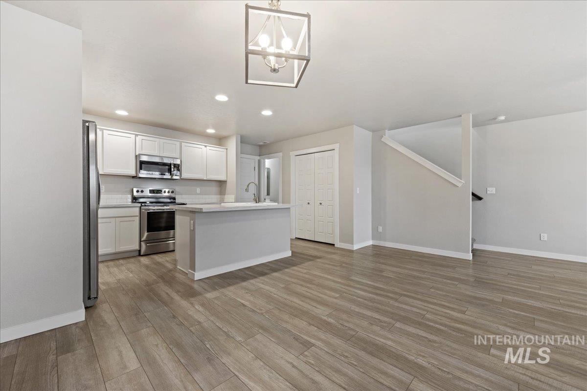2479 East Goldstone Street Meridian, ID 83642 - Photo 9 of 29 Kitchen featuring stainless steel appliances, an island with sink, white cabinetry, light wood finished floors, and suspended lighting