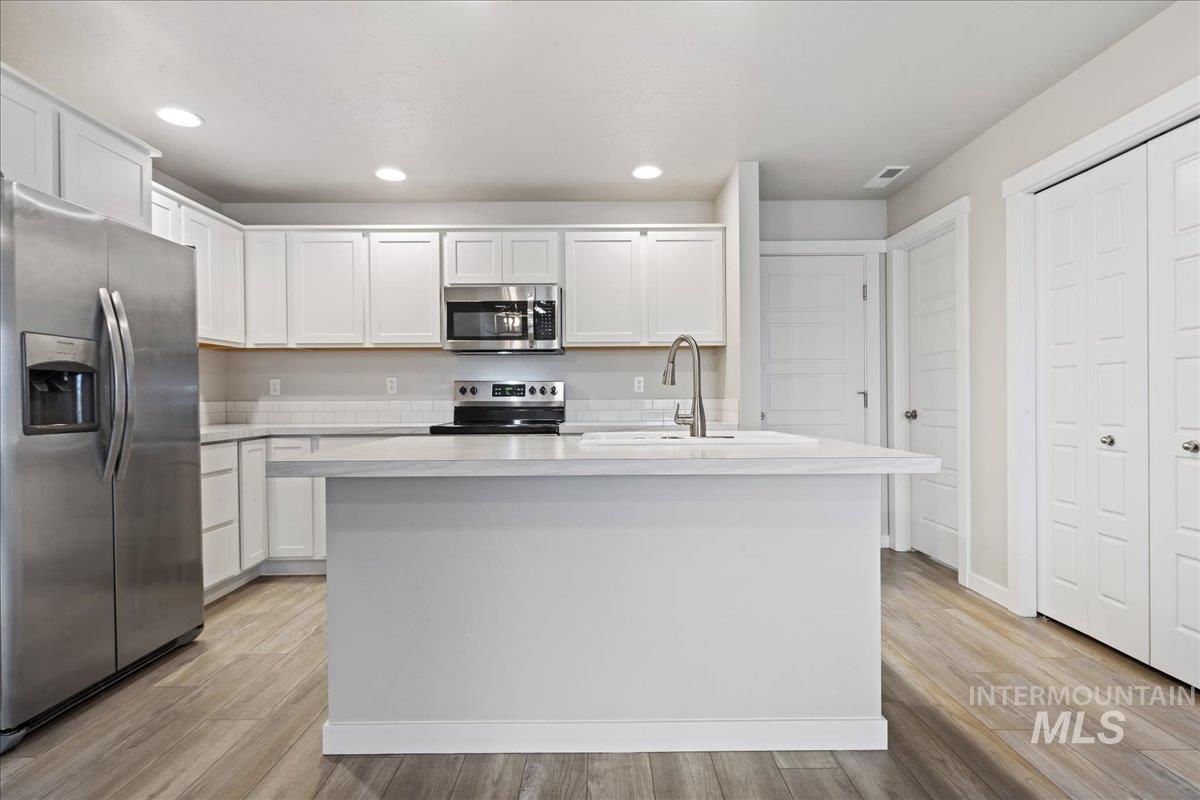 2479 East Goldstone Street Meridian, ID 83642 - Photo 10 of 29 Kitchen featuring stainless steel appliances, white cabinetry, light wood-type flooring, a kitchen island with sink, and recessed lighting