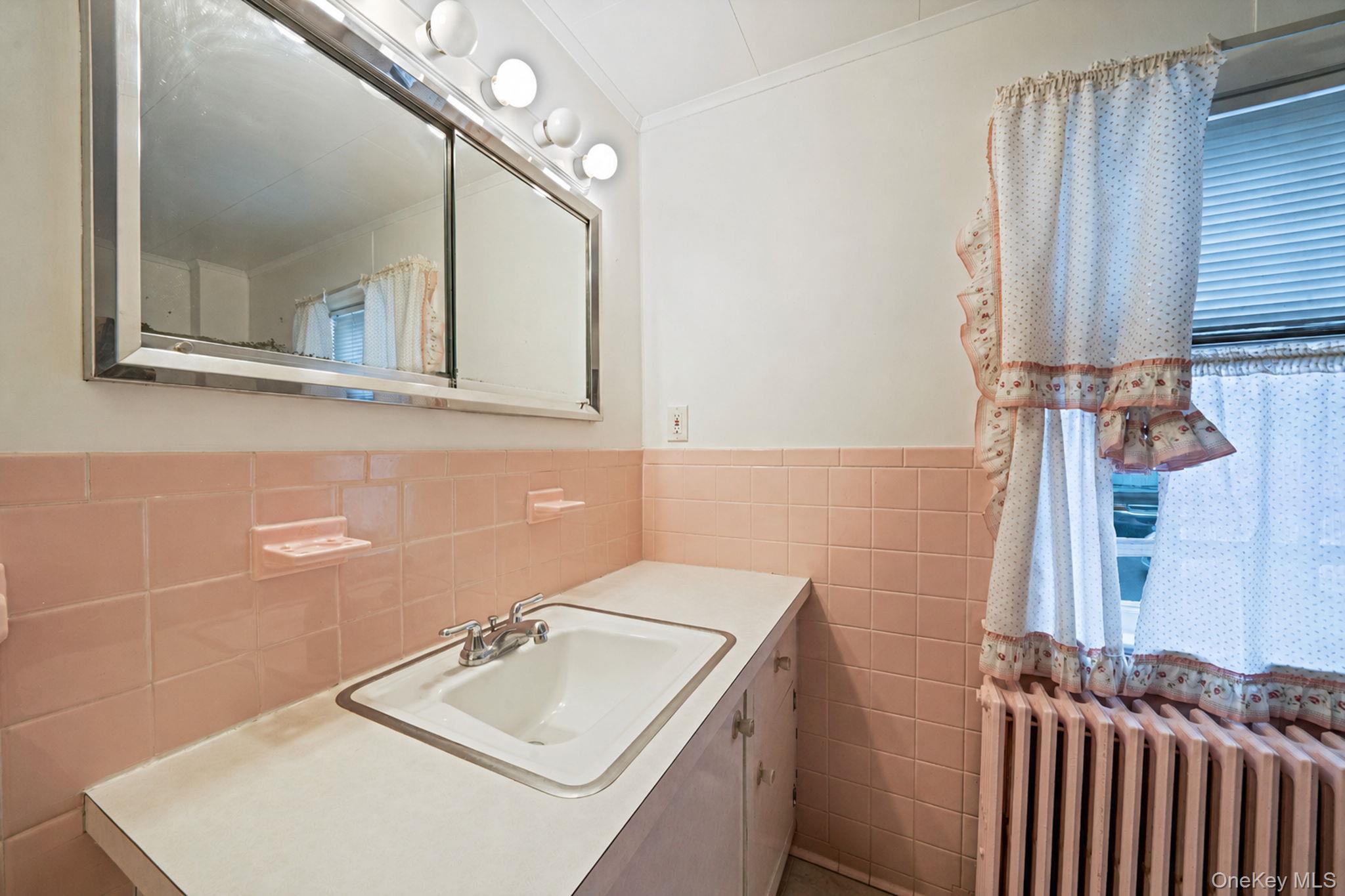 1055 Oregon Road Mattituck, NY 11952 - Photo 18 of 33 Bathroom featuring pink tiled wainscoting, a wall-mounted vanity mirror with integrated lighting, a drop-in sink with a chrome faucet, r