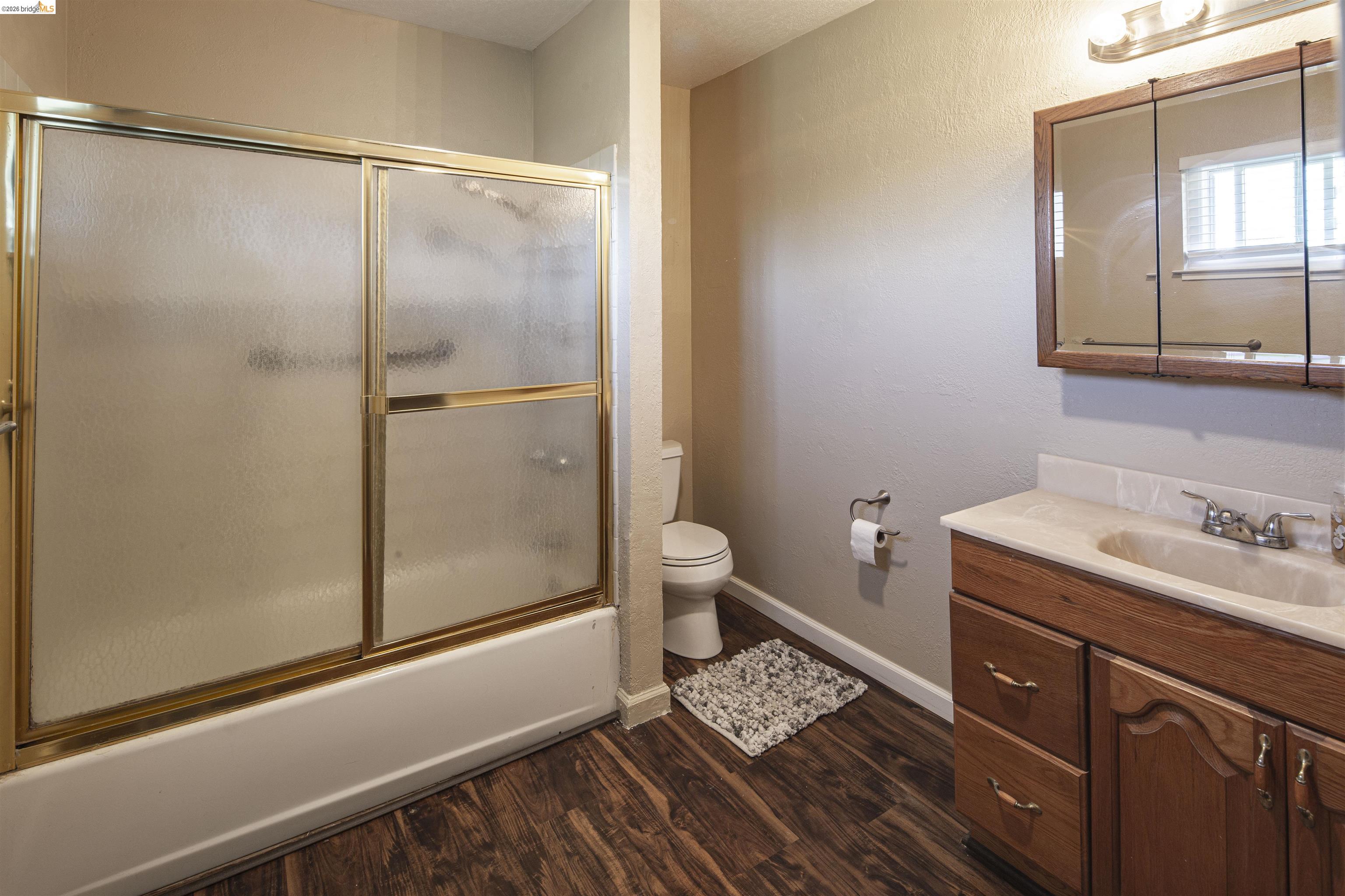 10458 Southworth Road Valley Springs, CA 95252 - Photo 14 of 22 Bathroom with vanity, a textured wall, dark wood finished floors, and bath / shower combo with glass door