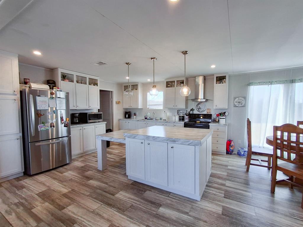 7256 Johnson Road Granbury, TX 76049 - Photo 15 of 40 Kitchen featuring light countertops, freestanding refrigerator, white cabinets, decorative light fixtures, and wall chimney exhaust hood