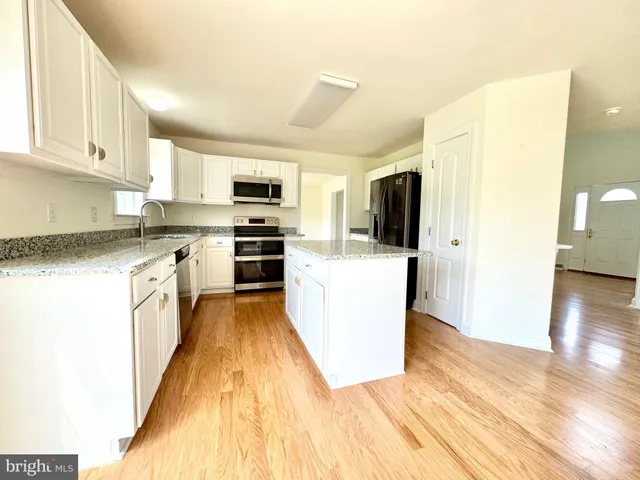 a kitchen with stainless steel appliances a stove top oven a sink a refrigerator white cabinets and wooden floor