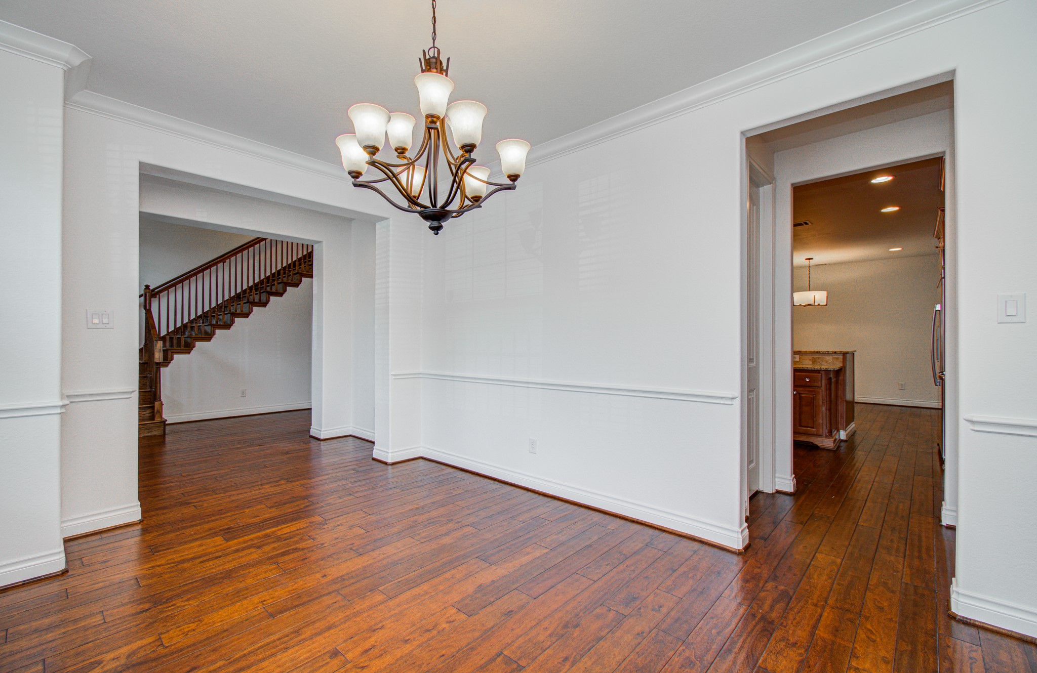6621 North Main Street Houston, TX 77009 - Photo 6 of 41 Home showcases a bright, open dining area with elegant hardwood floors and a stylish chandelier. It features white walls with wainscoting, and offers views into a kitchen and staircase, providing a spacious and connected feel.