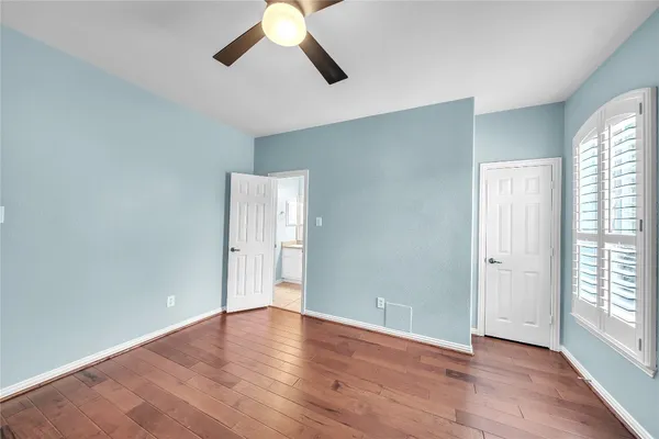 an empty room with wooden floor chandelier fan and windows