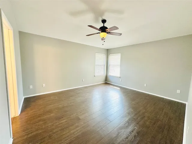 an empty room with wooden floor fan and windows