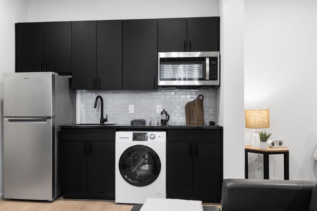 596 West 9th Street, Unit 339 Dallas, TX 75208 - Photo 16 of 22 Kitchen featuring dark cabinetry, washer / clothes dryer, stainless steel appliances, and backsplash