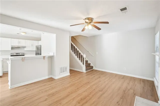 a view of an empty room with wooden floor and a kitchen view