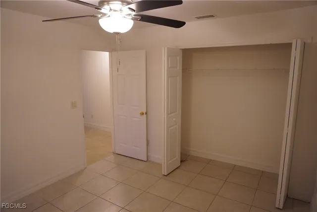 an empty room with a chandelier fan and kitchen view