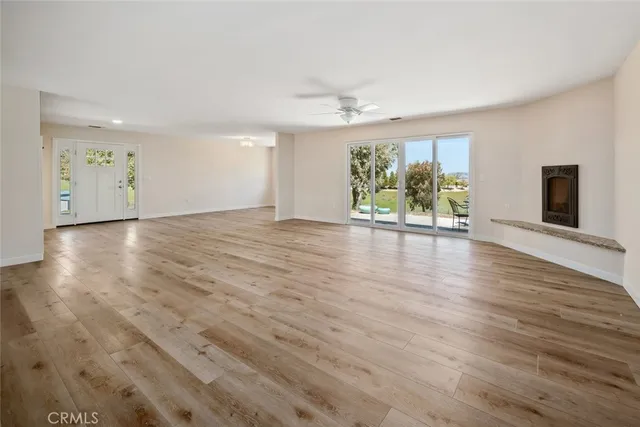 an empty room with wooden floor chandelier fan and windows